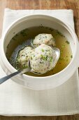 Clear broth with bacon dumplings in soup bowl with spoon