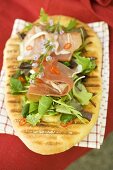 Woman holding pizza bread topped with Parma ham, herbs, chilli rings