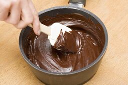 Geschmolzene Schokolade mit Teigschaber im Kochtopf verrühren