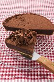 Chocolate tart on cake rack and piece on cake server