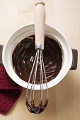 Remains of chocolate sauce in pot and on whisk