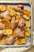 Roast chicken pieces with oranges on baking tray