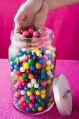 Hand taking coloured bubble gum balls out of jar