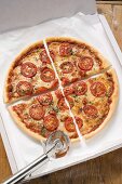 Pizza mit Tomaten, Käse, Oregano (geviertelt) im Pizzakarton