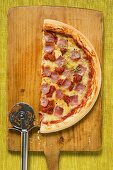 Halbe Pizza mit Schinken, Tomaten und Käse auf Schneidebrett