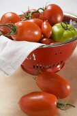 Various types of tomatoes in colander, two beside it