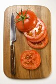 Tomatenscheiben und Messer auf Schneidebrett (Draufsicht)