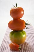 Various types of tomatoes on tea towel (in a pile)