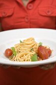 Woman holding plate of spaghetti with tomatoes and basil