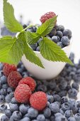 Blueberries and raspberries with leaves, some in bowl