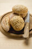 Baguette and wholemeal rolls on breadboard with knife