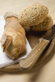 Baguette & wholemeal bread rolls on breadboard with knife