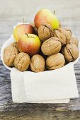 Walnuts and apples on cloth in white bowl