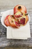 Pomegranate, whole and halved, on cloth in white bowl