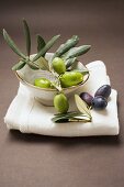 Olive sprig with green olives in bowl, black olives on cloth