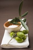 Olive sprig with green olives, sea salt in terracotta bowl