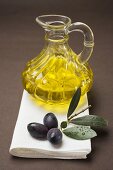 Schwarze Oliven am Zweig, dahinter Olivenöl in Karaffe