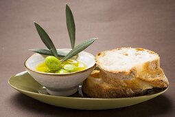 Olive sprig with green olives in bowl of olive oil, white bread