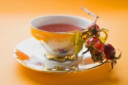 Rose hip tea in china cup, fresh rose hips in saucer