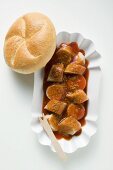 Sausage with ketchup & curry powder in paper dish, bread roll