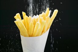 Pommes frites in Papiertüte mit Salz bestreuen