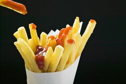 Pommes frites mit Ketchup in Papiertüte und darüber