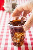 Hand reaching for plastic beaker of cola