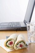 Thunfisch-Wraps und Mineralwasser vor Laptop