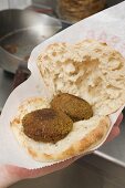 Hand holding pita bread filled with falafel (chick-pea balls)