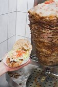 Hand holding a döner kebab (opened), meat on spit