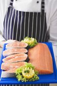 Person holding various cuts of salmon on chopping board