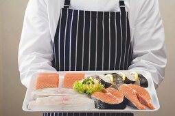 Person hält Tablett mit Lachs- und Wolfsbarschstücken