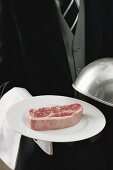 Butler serving raw beef steak on plate with dome cover