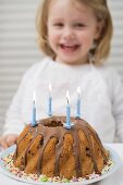 Small girl behind birthday cake with candles