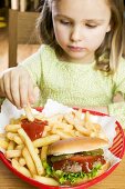 Mädchen isst Pommes frites mit Ketchup und Hamburger