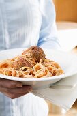 Woman holding plate of spaghetti with meatballs