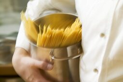 Koch läuft mit Spaghetti im Kochtopf durch Küche
