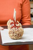 Woman holding a tray of toffee apples with chopped nuts