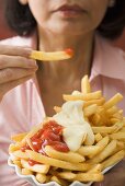 Frau isst Pommes frites mit Ketchup und Mayonnaise
