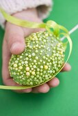 Child's hand holding green decorated Easter egg