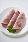 Three slices of Schinkenwurst (ham sausage) with parsley on plate