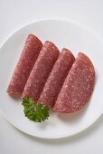 Four slices of salami with parsley on plate