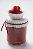Jar of raspberry jam, raspberries in paper case on top