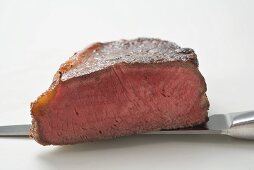 Beef steak, showing cut edge, on knife