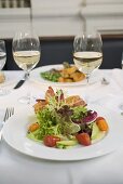 Salad with bacon and glasses of white wine on laid table