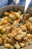 Fried potatoes with vegetables & bacon in frying pan with spoon