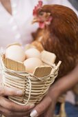 Woman holding live hen and basket of eggs