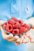 Child's hands holding glass dish of raspberries