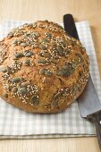 Wholemeal bread with pumpkin seeds on tea towel with bread knife