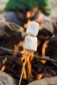 Marshmallows am Spiess vor Lagerfeuer, Mensch im Hintergrund
